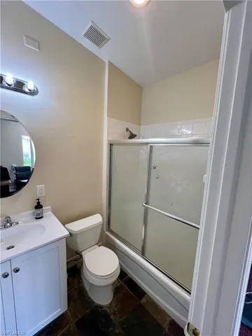 Full bathroom featuring toilet, vanity, bath / shower combo with glass door, and visible vents
