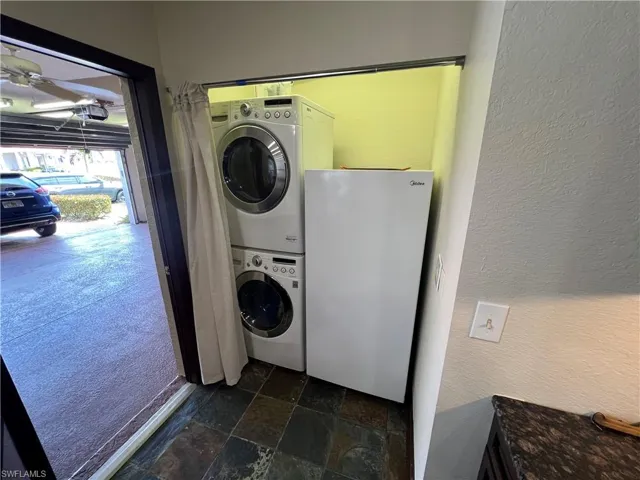 Washroom featuring stone tile flooring, a textured wall, a ceiling fan, and stacked washer and clothes dryer