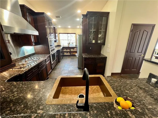 Kitchen with a sink, visible vents, glass insert cabinets, wall chimney range hood, and appliances with stainless steel finishes