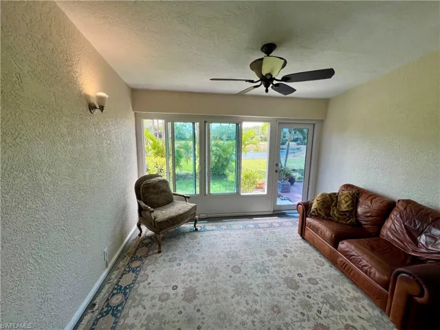 Carpeted living area with a textured wall, a textured ceiling, a ceiling fan, and baseboards