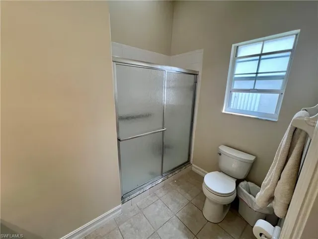 Full bathroom with a shower stall, toilet, tile patterned floors, and baseboards