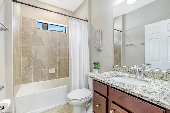 Full bathroom featuring vanity, granite countertops shower / tub combo with curtain, and light tile patterned floors