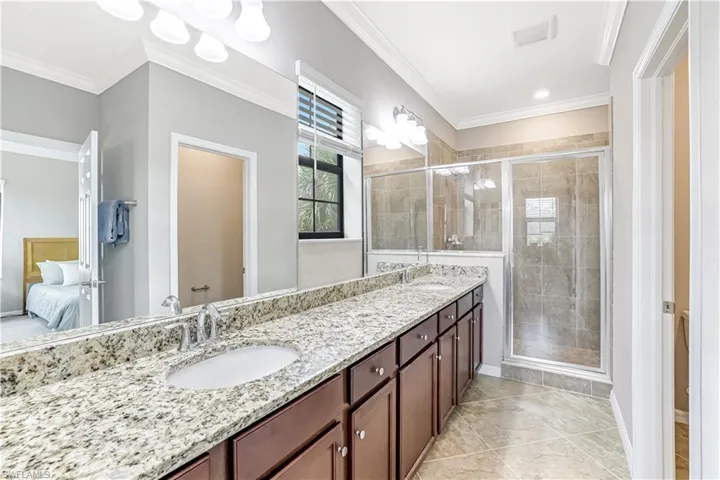 Master Ensuite Bathroom with crown molding, double vanity, granite countertops, a stall shower, tile floors, and a large walk-in closet