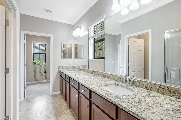 Master Ensuite Bathroom with crown molding, double vanity, granite countertops, a stall shower, tile floors, and a large walk-in closet