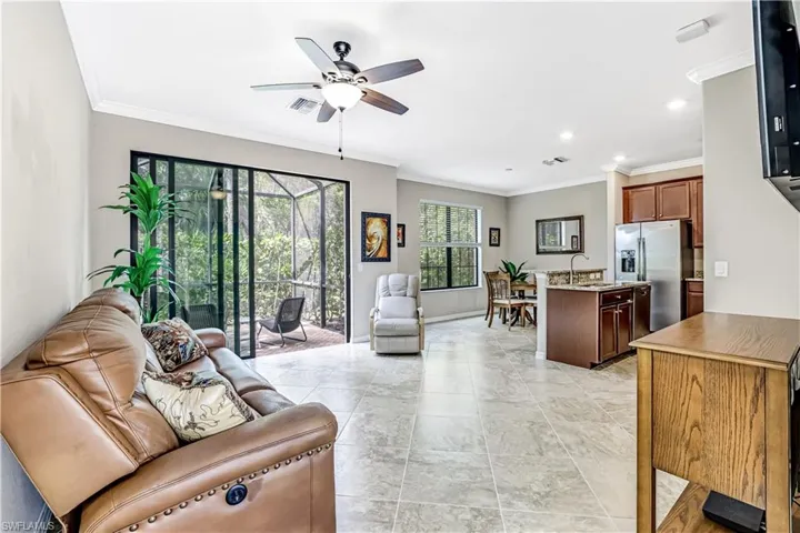 Spacious, open living room with crown molding, ceiling fan, and access to large kitchen and screened patio/lanai