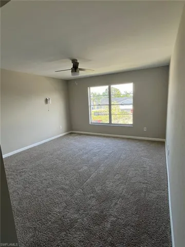 Empty room with carpet flooring, a ceiling fan, and baseboards