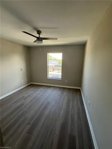 Spare room featuring dark wood-style floors, ceiling fan, and baseboards