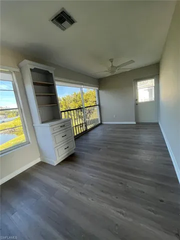 Unfurnished room with baseboards, dark wood-style floors, visible vents, and a ceiling fan