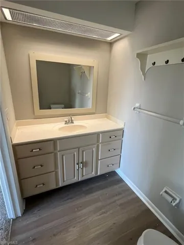 Half bath featuring baseboards, wood finished floors, toilet, and vanity