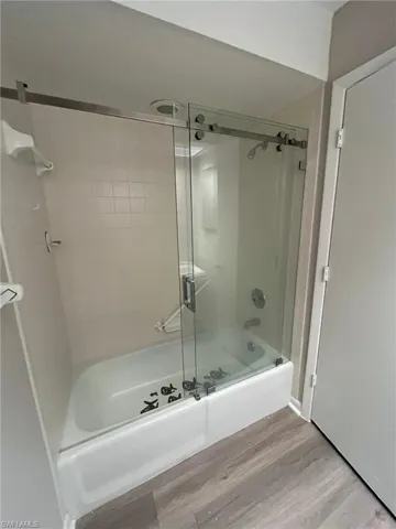 Bathroom featuring bath / shower combo with glass door and wood finished floors