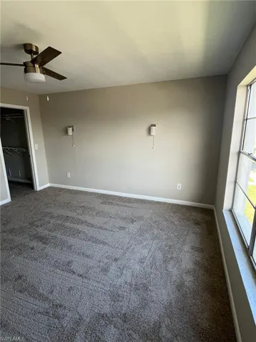 Empty room with baseboards, dark colored carpet, and ceiling fan