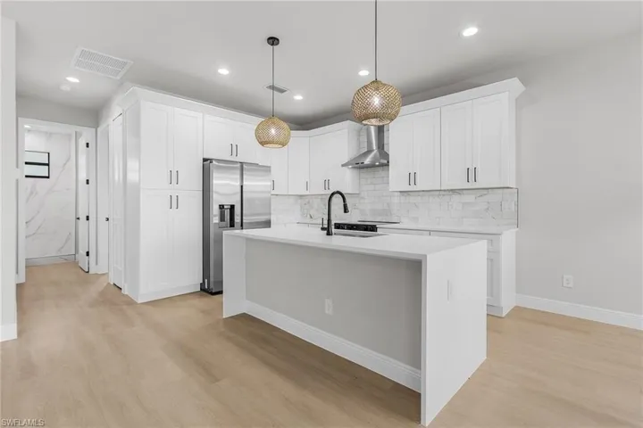 Kitchen featuring stainless steel refrigerator with ice dispenser, tasteful backsplash, light wood-type flooring, light countertops, and wall chimney range hood