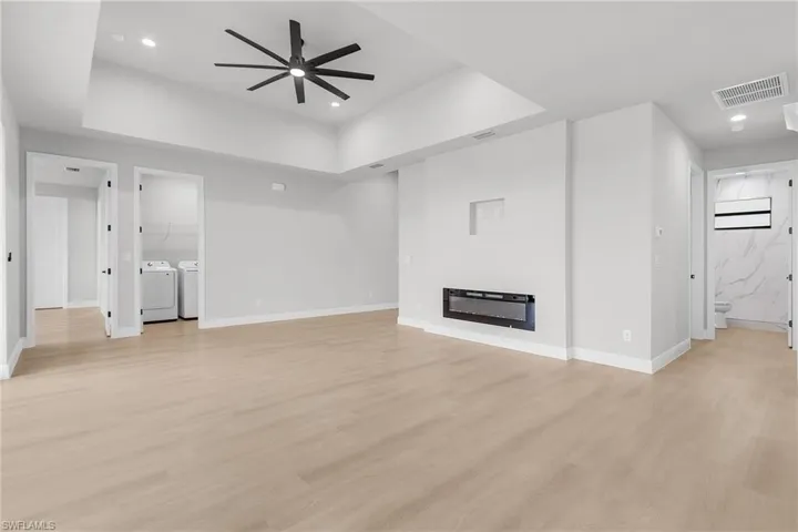 Unfurnished living room featuring washing machine and clothes dryer, a tray ceiling, ceiling fan, light wood-style flooring, and recessed lighting