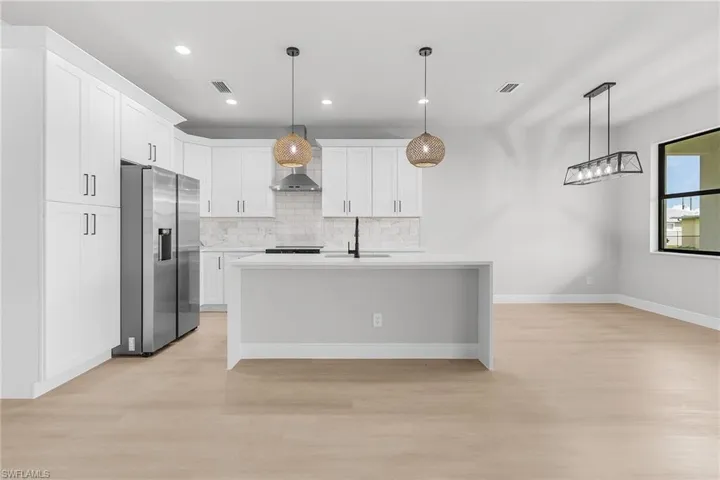 Kitchen featuring stainless steel refrigerator with ice dispenser, light wood finished floors, wall chimney exhaust hood, decorative backsplash, and recessed lighting