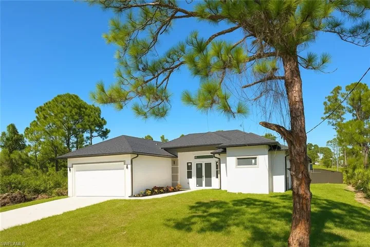 View of front of home with a front yard, stucco siding, a garage, and driveway