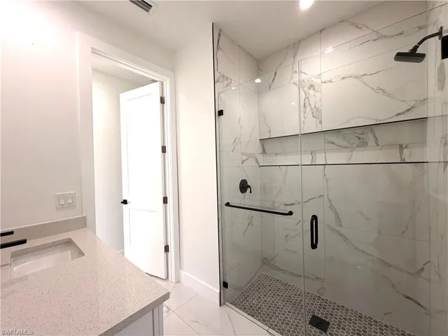 Full bathroom with vanity, a marble finish shower, and light tile patterned floors