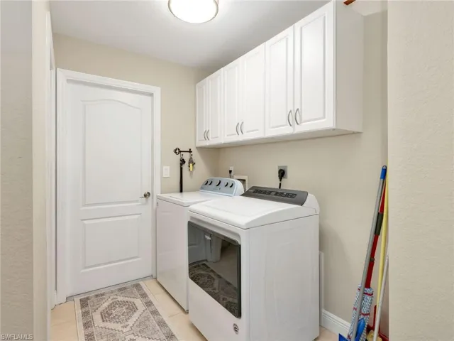 Laundry area featuring cabinet space, a textured wall, washing machine and dryer, and light tile patterned floors