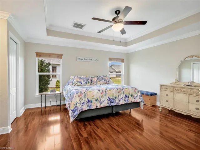 Bedroom with wood finished floors, a tray ceiling, ceiling fan, and ornamental molding