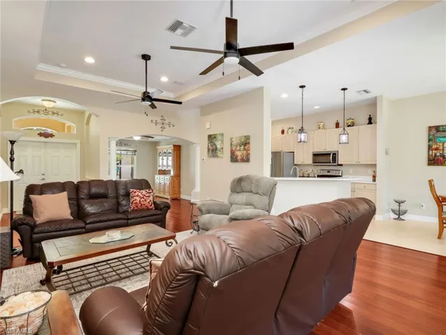 Living room with arched walkways, light wood-style flooring, a raised ceiling, a ceiling fan, and crown molding