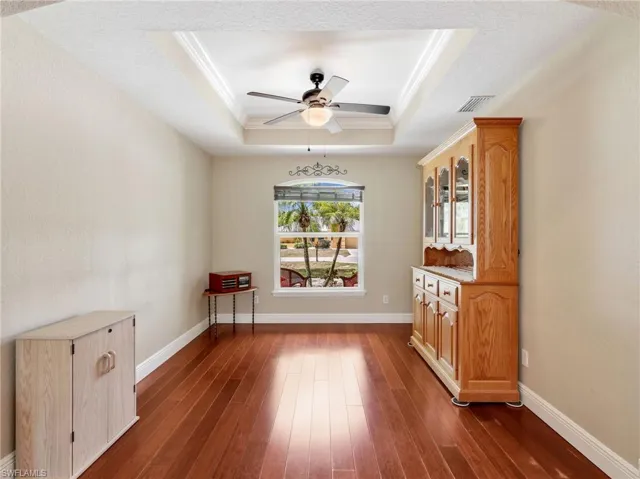 Unfurnished room featuring ornamental molding, a ceiling fan, dark wood-type flooring, and a tray ceiling
