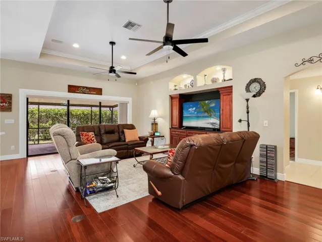 Living room featuring ornamental molding, arched walkways, hardwood / wood-style floors, recessed lighting, and a raised ceiling
