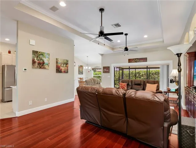 Living room featuring a tray ceiling, light wood-style flooring, plenty of natural light, ceiling fan, and ornamental molding