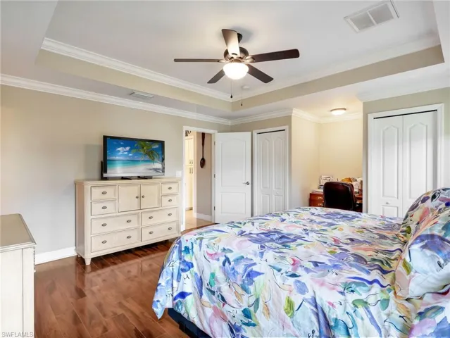 Bedroom with two closets, dark wood-style flooring, ornamental molding, a ceiling fan, and a tray ceiling