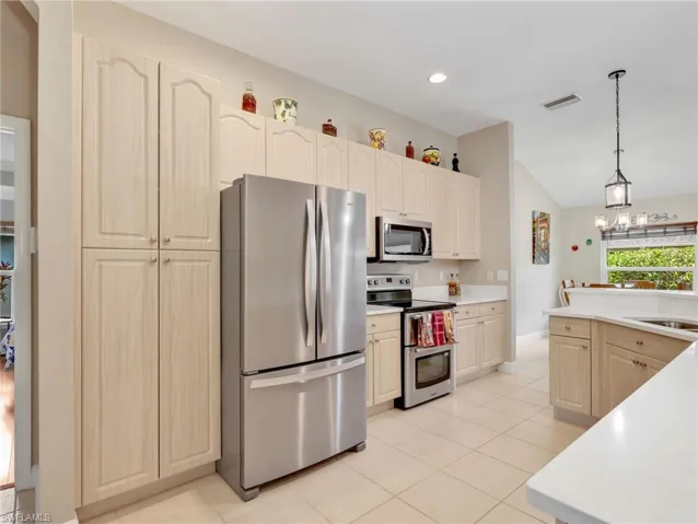 Kitchen with stainless steel appliances, lofted ceiling, light tile patterned floors, light wood finish cabinetry, and hanging lights