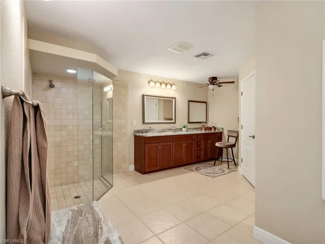 Bathroom featuring double vanity, a stall shower, light tile patterned flooring, and a ceiling fan