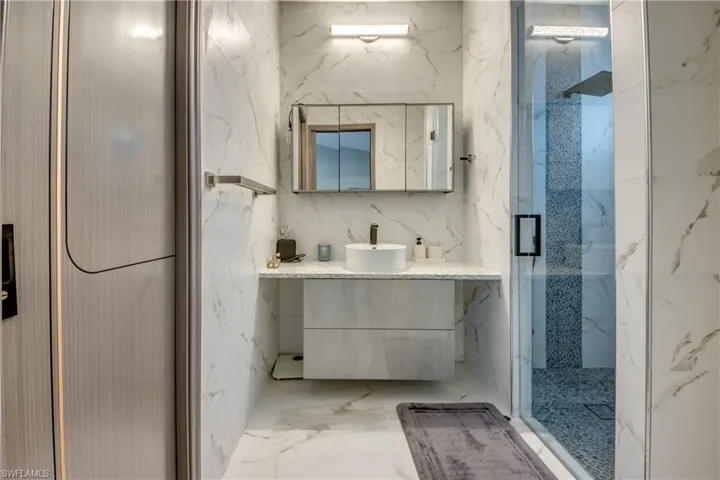 Bathroom featuring vanity, a marble finish shower, marble tiled floors, stone wall, and tile walls