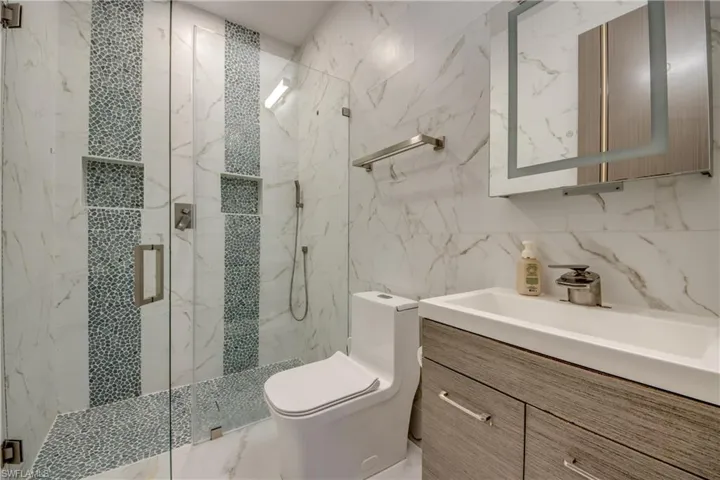 Full bathroom featuring tile walls, a marble finish shower, vanity, and marble tiled floors