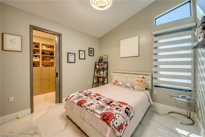 Bedroom with lofted ceiling, light marble finish flooring, and a walk in closet