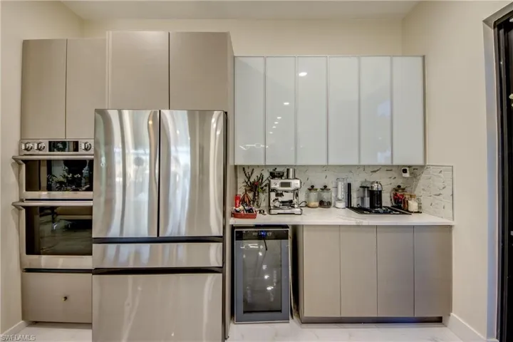 Kitchen featuring stainless steel appliances, modern cabinets, beverage cooler, backsplash, and white cabinets