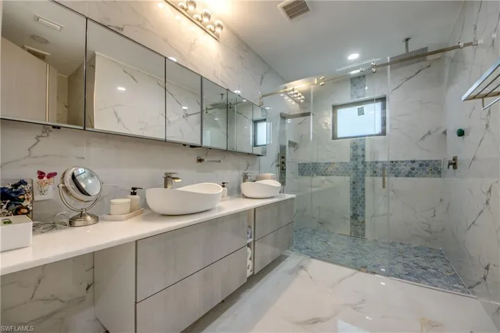 Bathroom featuring double vanity, a marble finish shower, light marble finish flooring, recessed lighting, and stone wall
