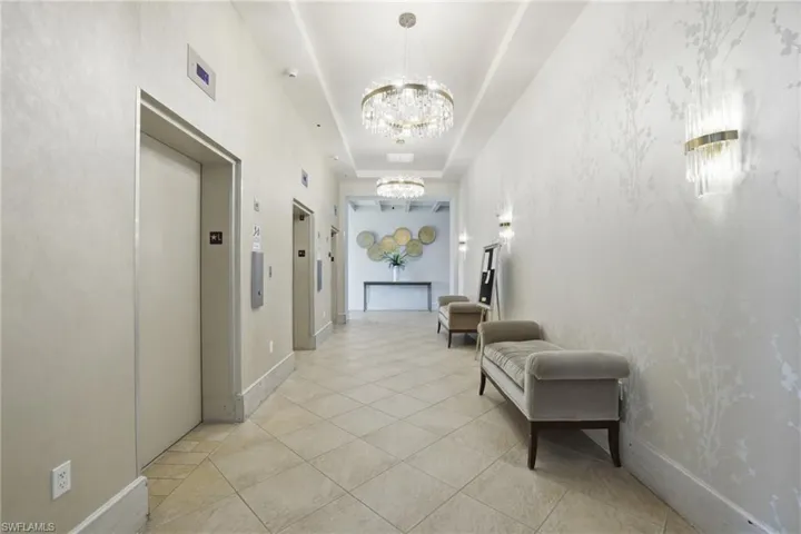 Corridor featuring a raised ceiling, elevator, light tile patterned floors, and a chandelier