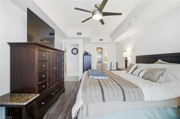 Bedroom featuring ornamental molding, dark wood finished floors, a ceiling fan, connected bathroom, and a tray ceiling