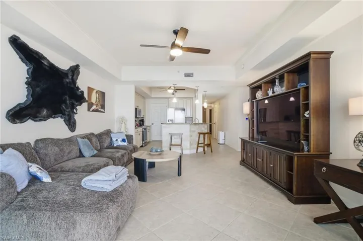 Living area featuring a ceiling fan, a tray ceiling, crown molding, and light tile patterned floors