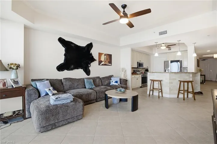 Living room with a raised ceiling, ceiling fan, light tile patterned floors, and crown molding