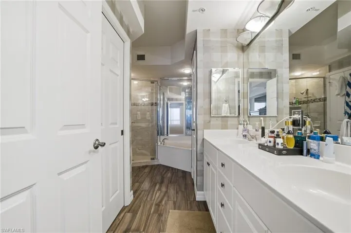Full bathroom featuring a bath, double vanity, a stall shower, and dark wood-type flooring
