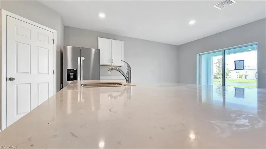 Kitchen with light stone countertops, stainless steel fridge, concrete floors, white cabinets, and sink