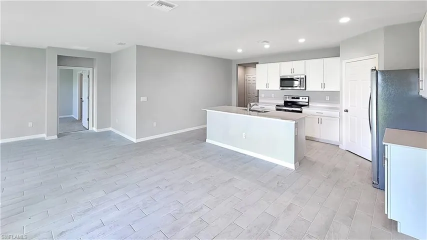 Kitchen with appliances with stainless steel finishes, white cabinetry, sink, and a center island with sink