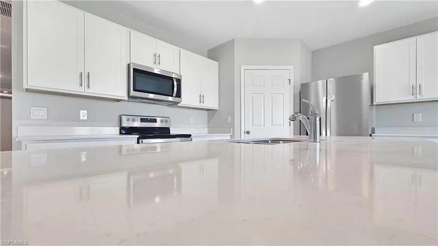 Kitchen with white cabinetry, sink, light stone counters, and stainless steel appliances