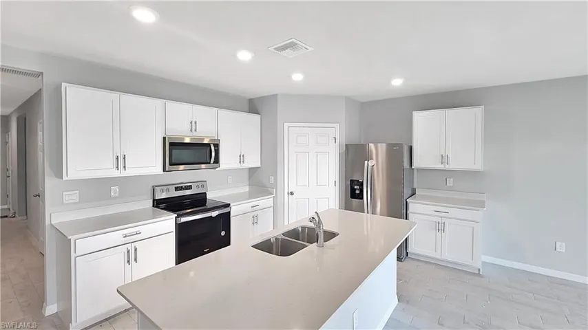 Kitchen with light hardwood / wood-style flooring, appliances with stainless steel finishes, white cabinets, a kitchen island with sink, and sink