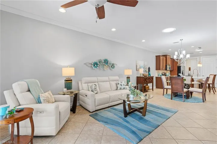 Tiled living room with ceiling fan with notable chandelier and crown molding