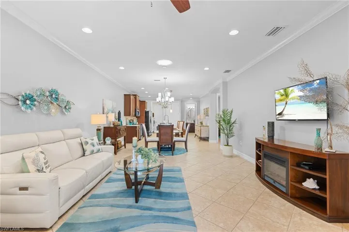 Living room featuring ceiling fan with notable chandelier, ornamental molding, and light tile patterned floors