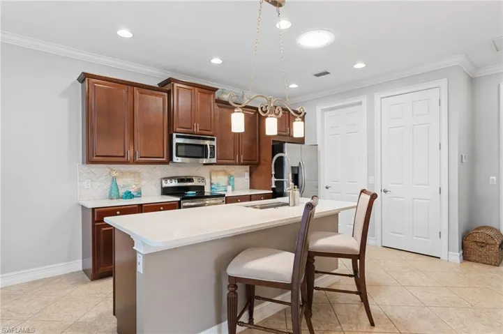 Kitchen with decorative backsplash, ornamental molding, stainless steel appliances, and an island with sink