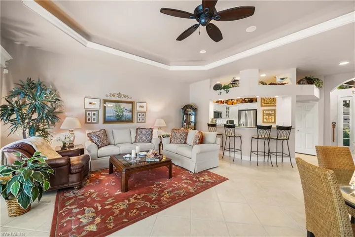 Living room featuring a ceiling fan, light tile patterned flooring, a tray ceiling, arched walkways, and recessed lighting