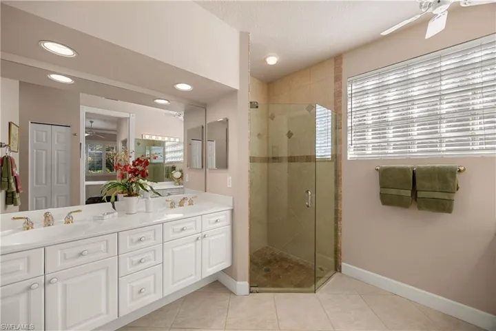 Primary Bathroom featuring ceiling fan, double vanity, a shower stall, light tile patterned flooring, and a textured ceiling