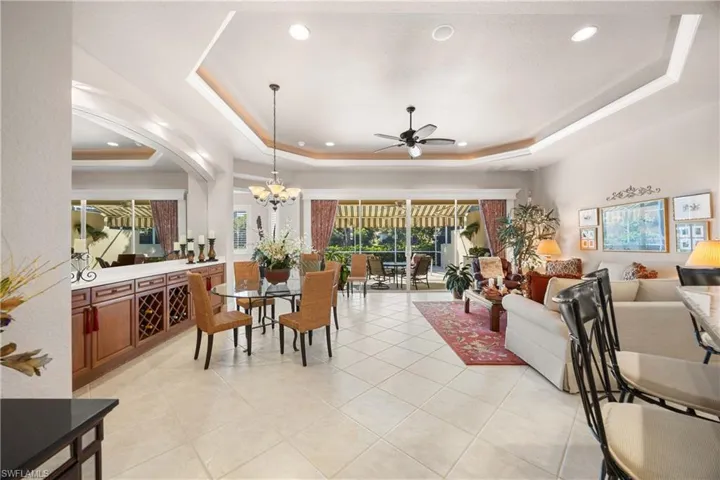 Dining area featuring a tray ceiling, light tile patterned floors, recessed lighting, a ceiling fan, and a chandelier