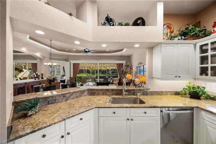 Kitchen with white cabinets, light stone counters, a textured wall, stainless steel dishwasher, and hanging light fixtures